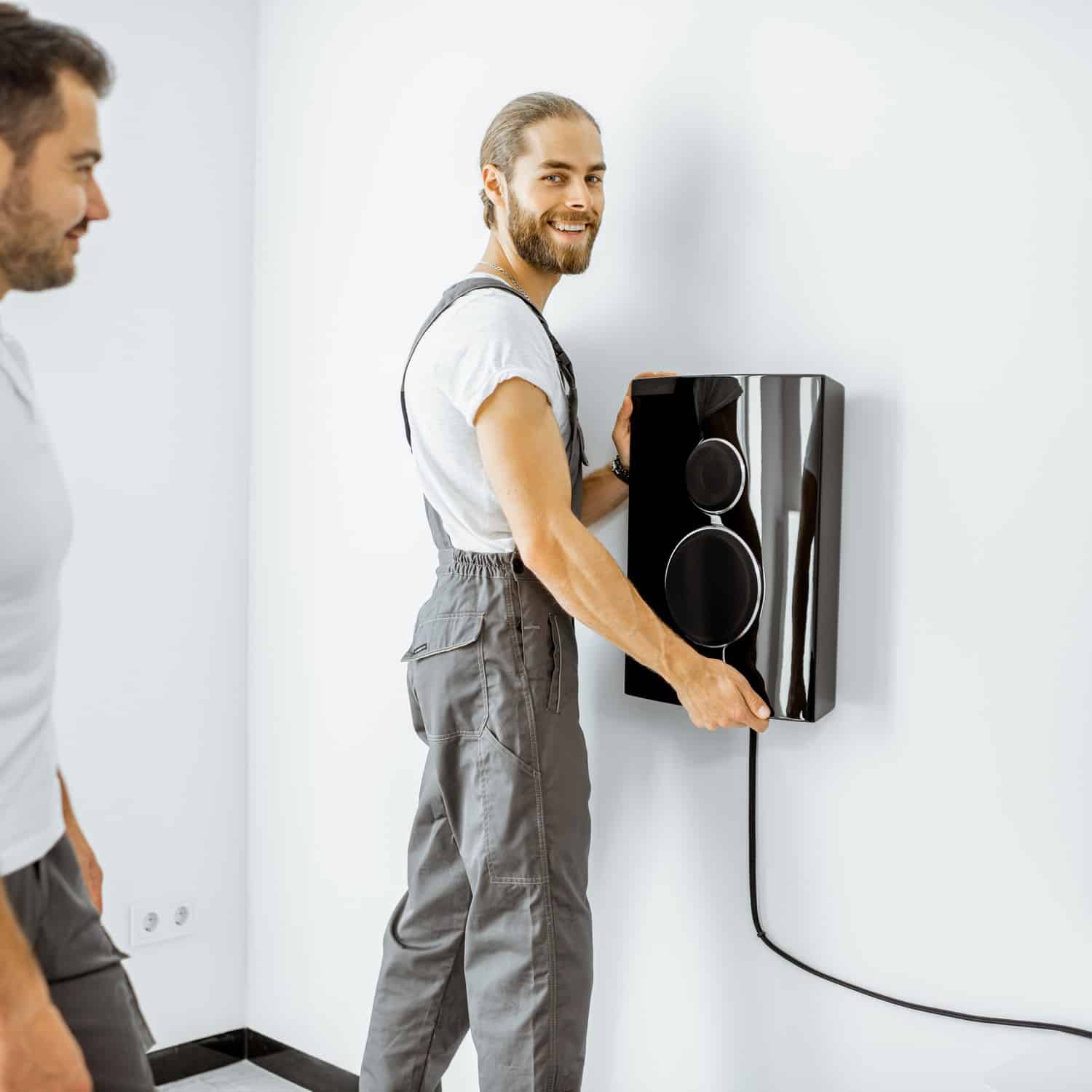 Two professional workmen in workwear installing luxury audio system in the white living room. Home appliances installation concept