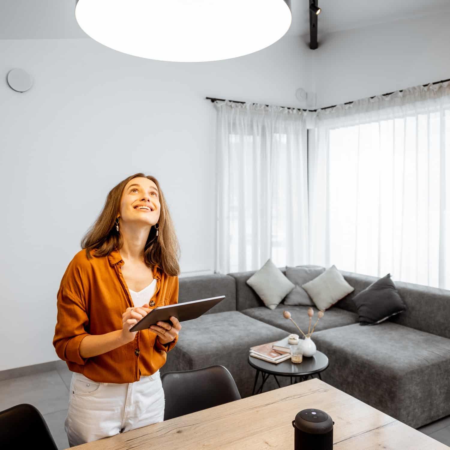 Young woman controlling home light with a digital tablet in the living room. Concept of a smart home and light control with mobile devices